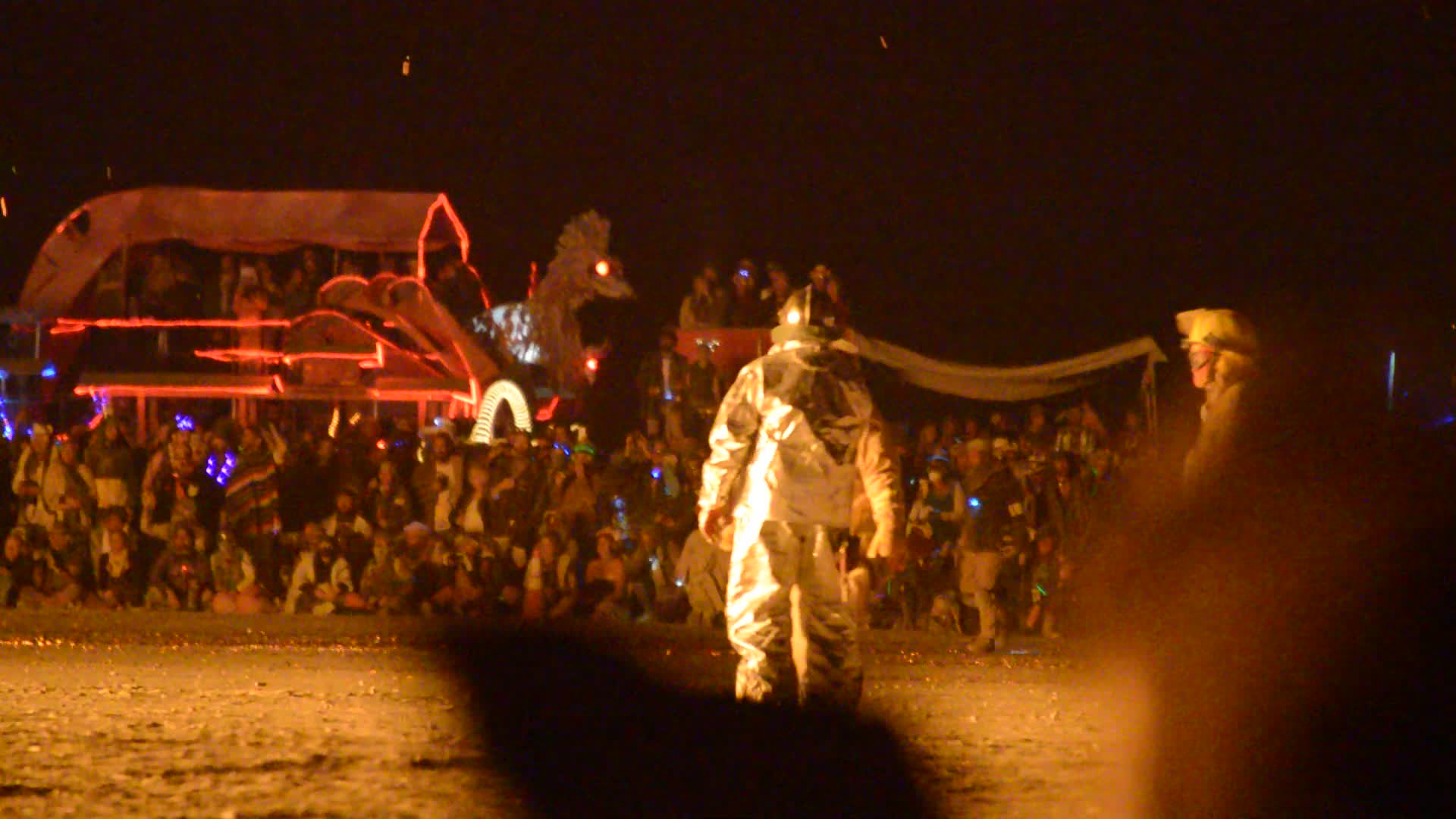 The Man structure burning at night surrounded by crowds at Burning Man festival