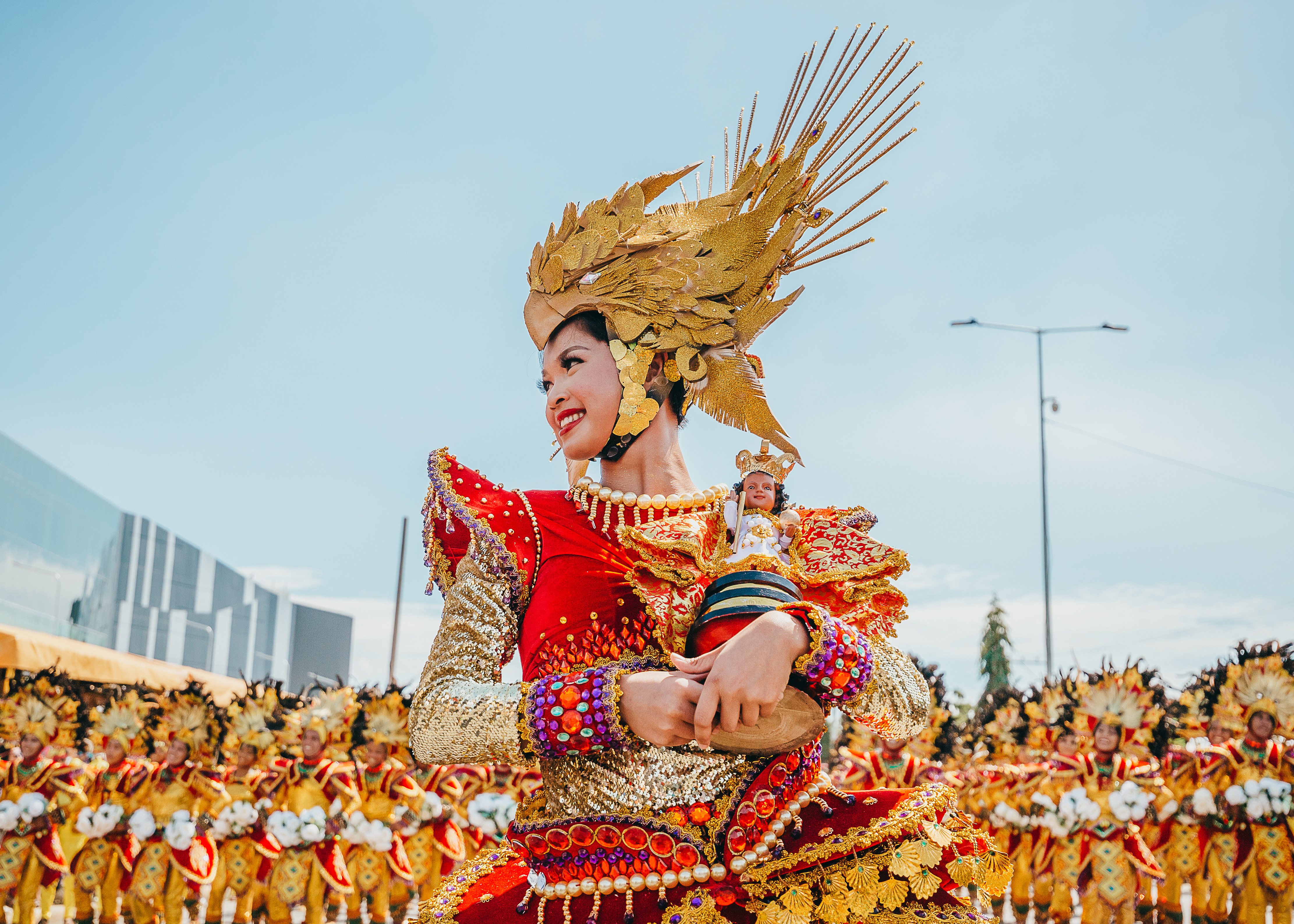 Thousands of costumed Sinulog dancers in bright reds and golds moving through the packed streets of Cebu City during the Grand Parade