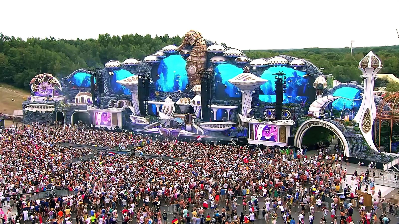 The vast, ornate Tomorrowland mainstage lit up at dusk above a huge crowd in the De Schorre park at Boom, Belgium